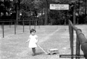 Die dreijährige Eva Hirche 1936 auf dem Alten Markt von Jever vor dem Plakat „Die Juden sind unser Unglück“. Es handelt sich um ein Einzelbild aus einem Schmalfilm, den der Vater in aufklärerischer Absicht drehte. (Foto A. Hirche)